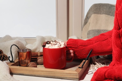 Woman with cup of cocoa at window, closeup. Winter drink