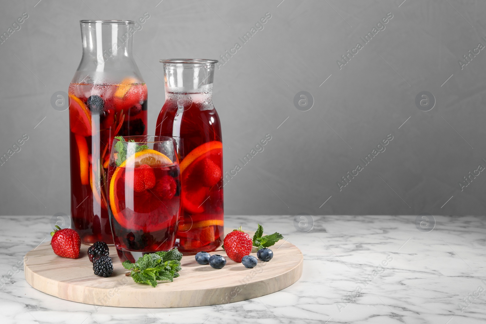 Photo of Delicious refreshing sangria and berries on white marble table, space for text