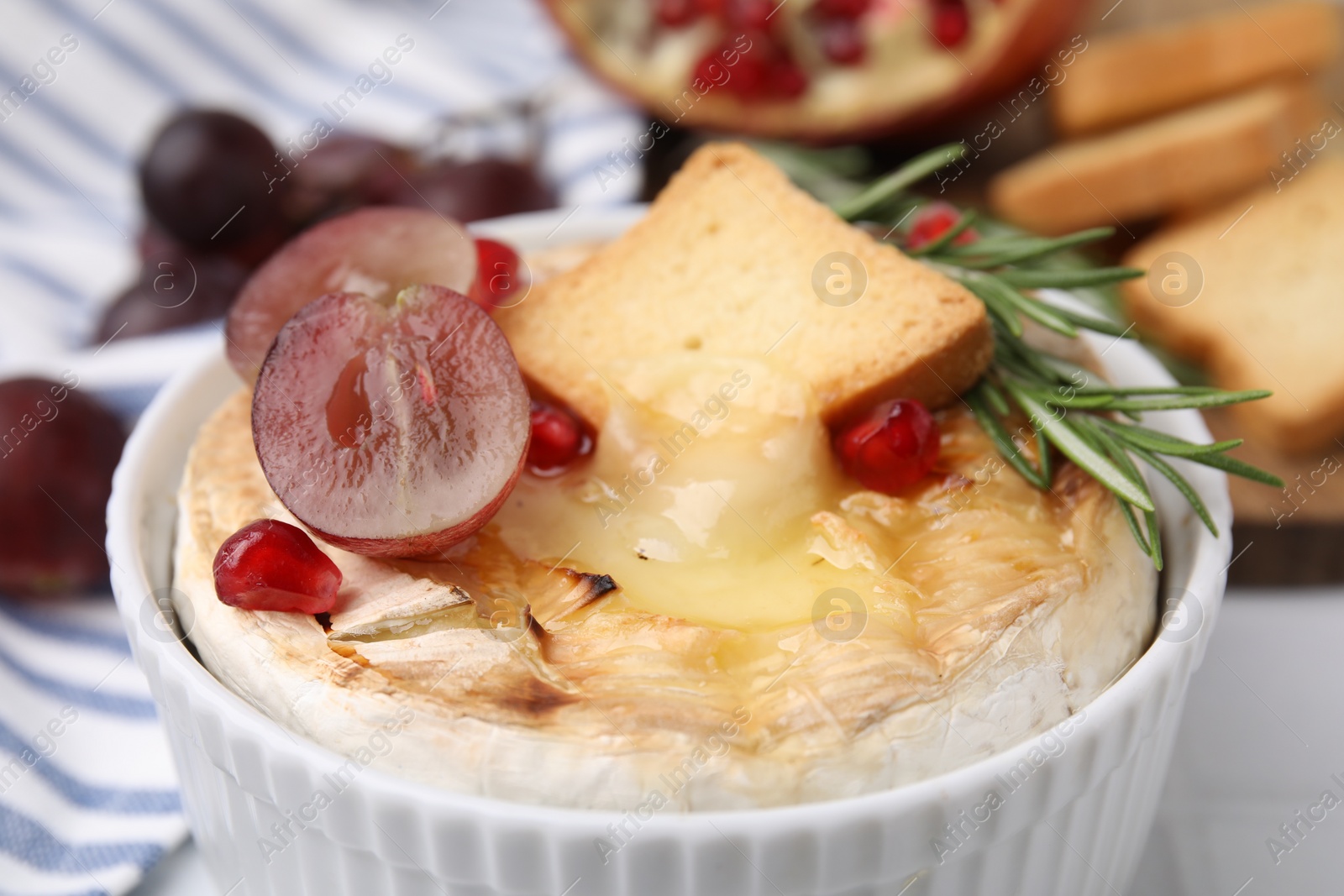 Photo of Tasty baked camembert with crouton, grape and rosemary on table, closeup