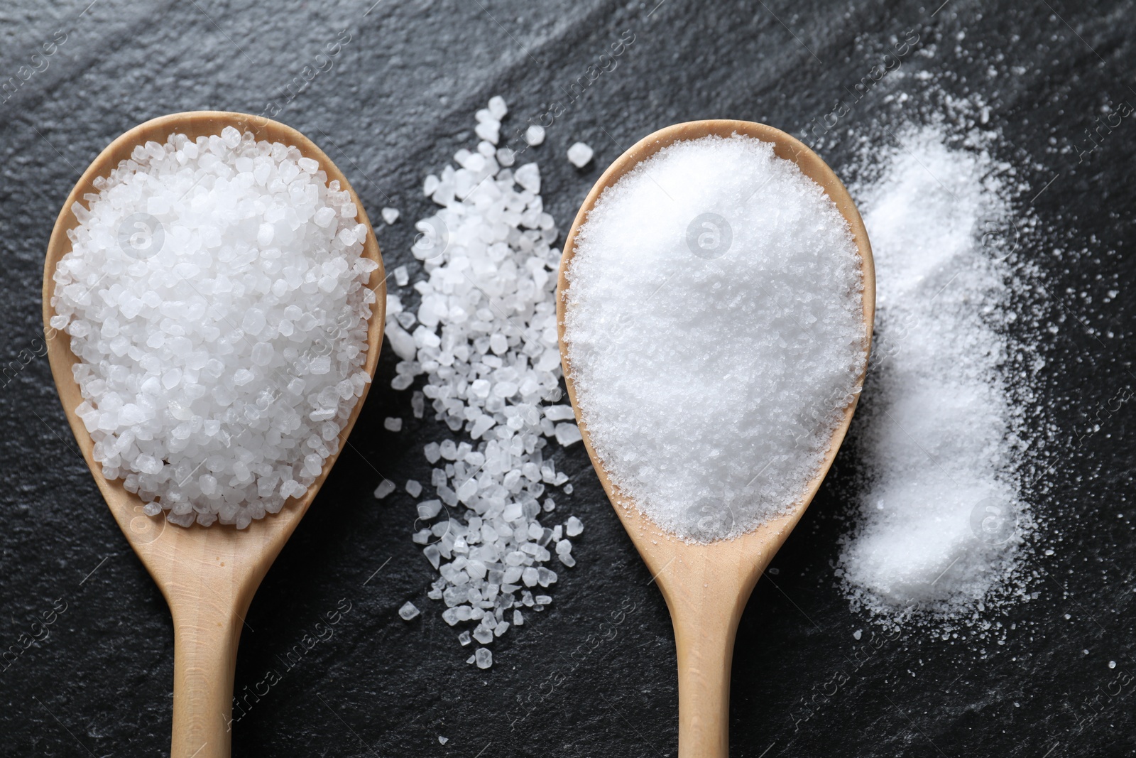 Photo of Organic salt in spoons on black table, flat lay