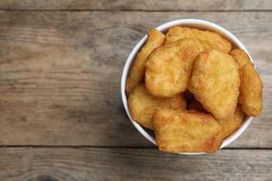 Bucket with tasty chicken nuggets on wooden table, top view. Space for text