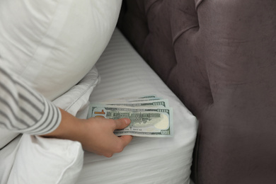 Photo of Woman hiding dollar banknotes under pillow in bedroom, closeup. Money savings