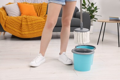 Woman dipping mop into bucket indoors, closeup