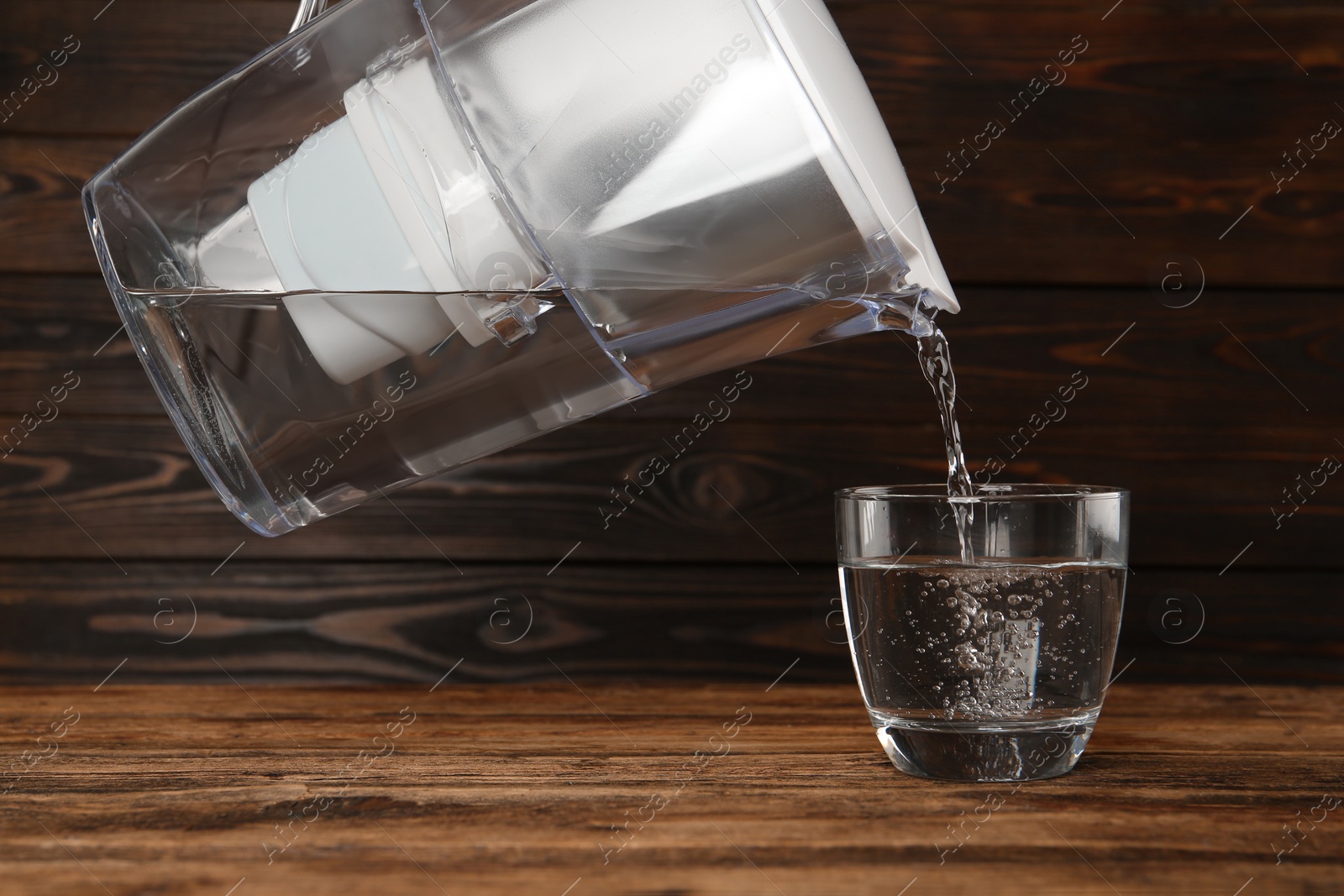 Photo of Pouring purified water from filter jug into glass on wooden table