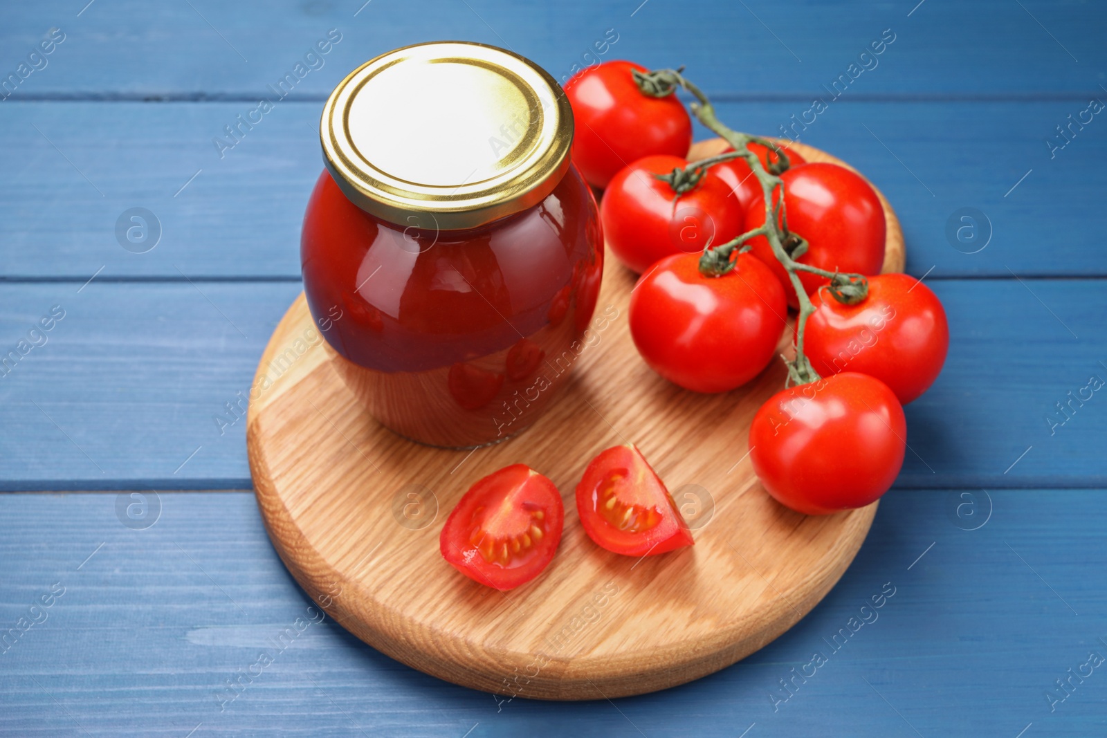 Photo of Organic ketchup in jar and fresh tomatoes on blue wooden table. Tomato sauce