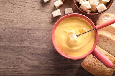 Photo of Flat lay composition with pot of cheese fondue and bread on wooden table, space for text