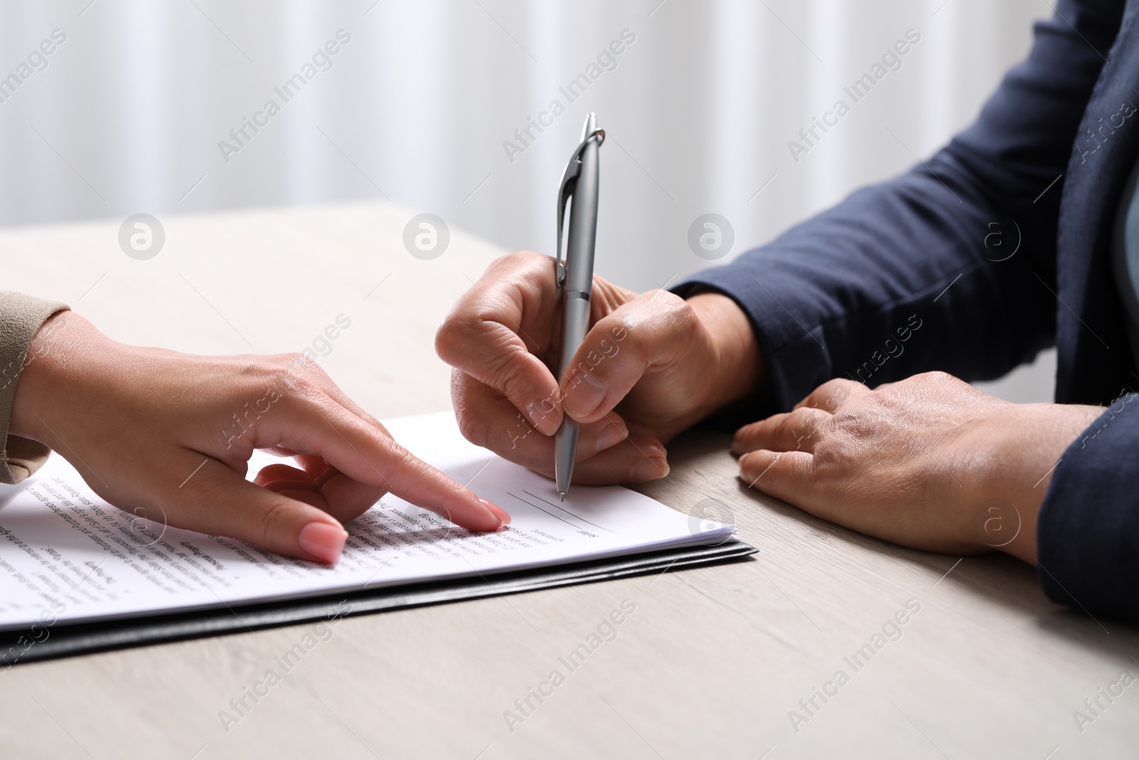 Photo of Manager showing client where she must to mark signature at light wooden table indoors, closeup