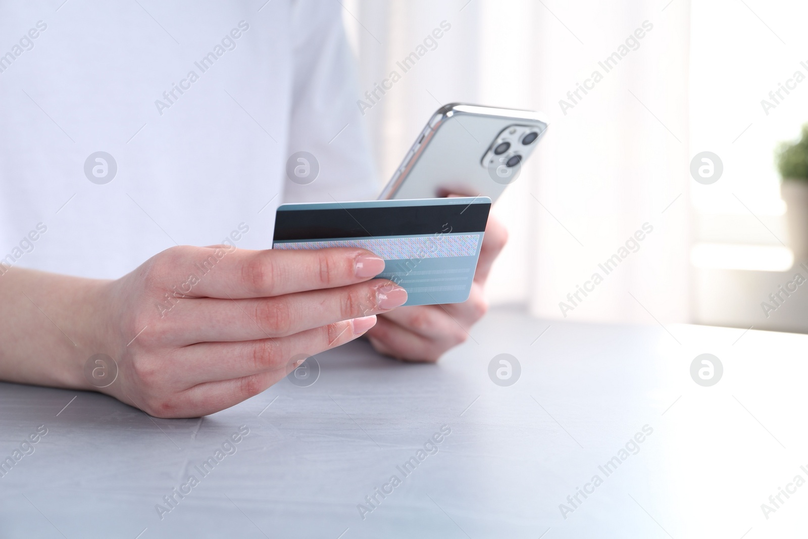 Photo of Online payment. Woman with smartphone and credit card at white table, closeup