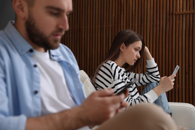 Photo of Couple addicted to smartphones ignoring each other at home. Relationship problems