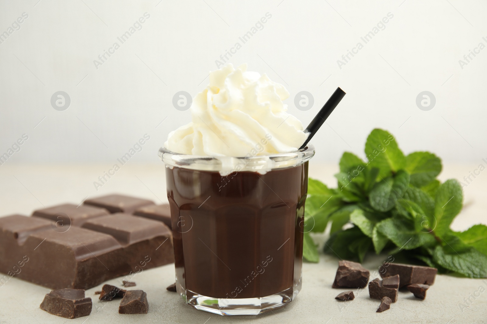Photo of Glass of delicious hot chocolate with whipped cream, chunks and fresh mint on light table