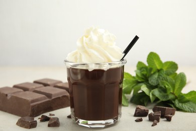 Photo of Glass of delicious hot chocolate with whipped cream, chunks and fresh mint on light table