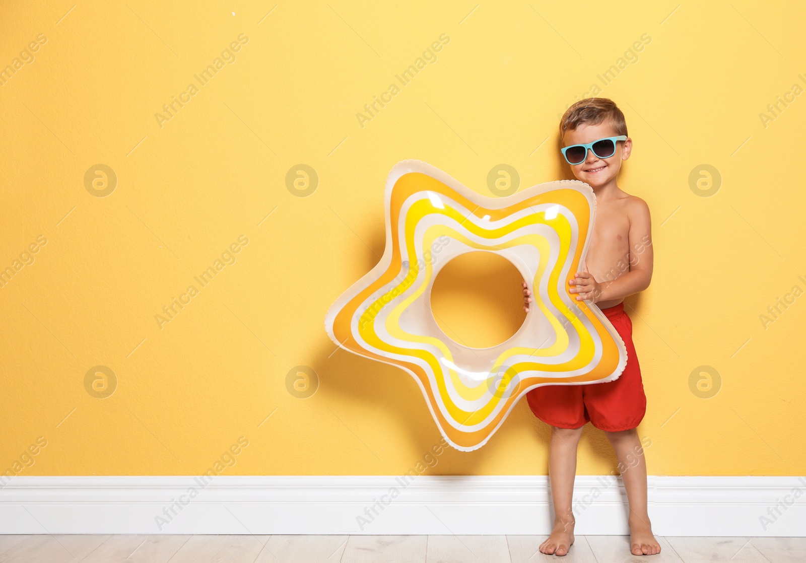 Photo of Cute little boy with bright star shaped inflatable ring near color wall