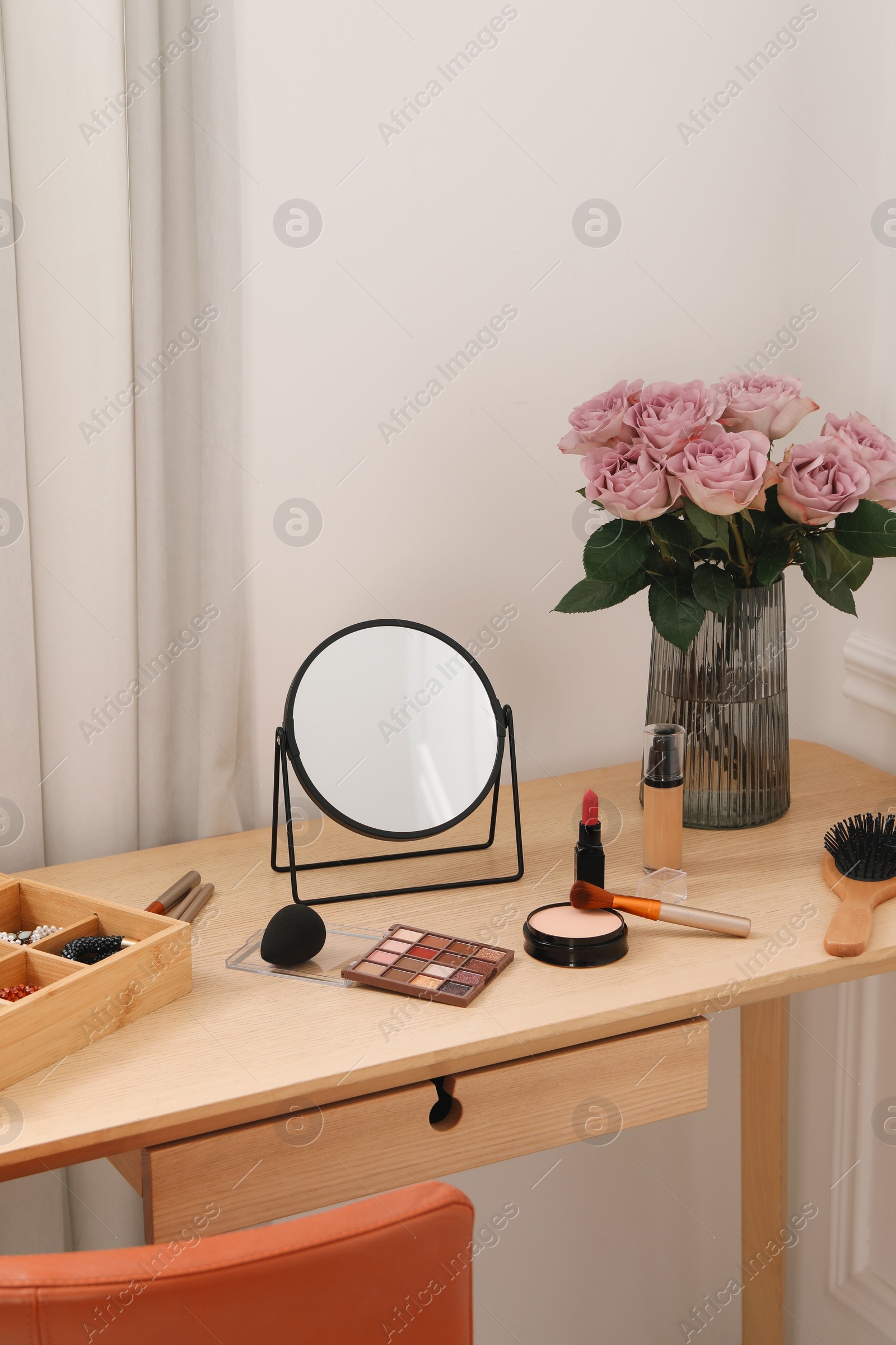 Photo of Mirror, cosmetic products, box of jewelry and vase with pink roses on wooden dressing table in makeup room