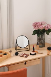 Mirror, cosmetic products, box of jewelry and vase with pink roses on wooden dressing table in makeup room