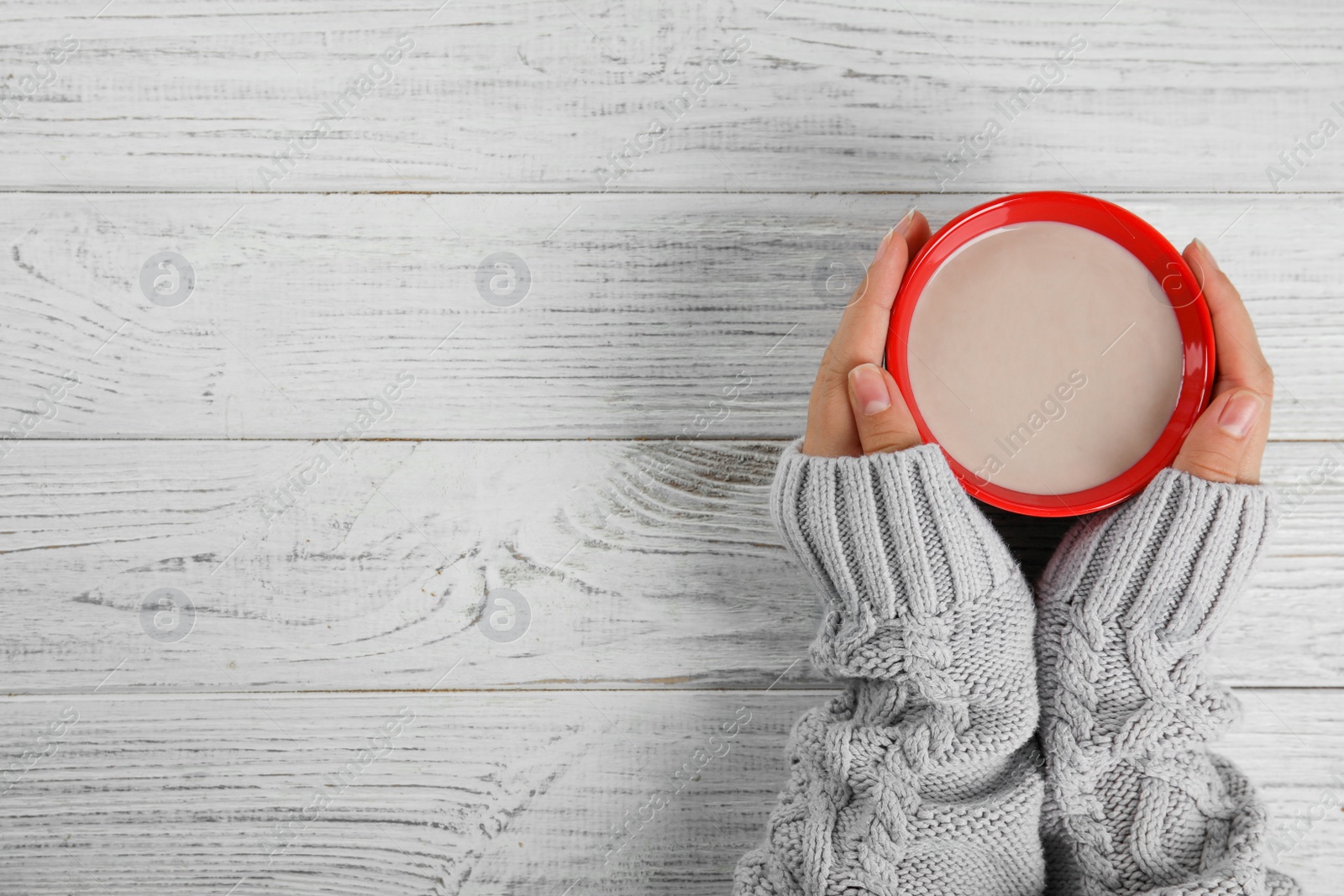 Photo of Woman holding cup of hot cocoa at white wooden table, top view with space for text. Winter drink