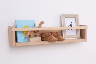 Photo of Wooden shelf with child's booties, toy, book and photo frame on white wall. Interior element