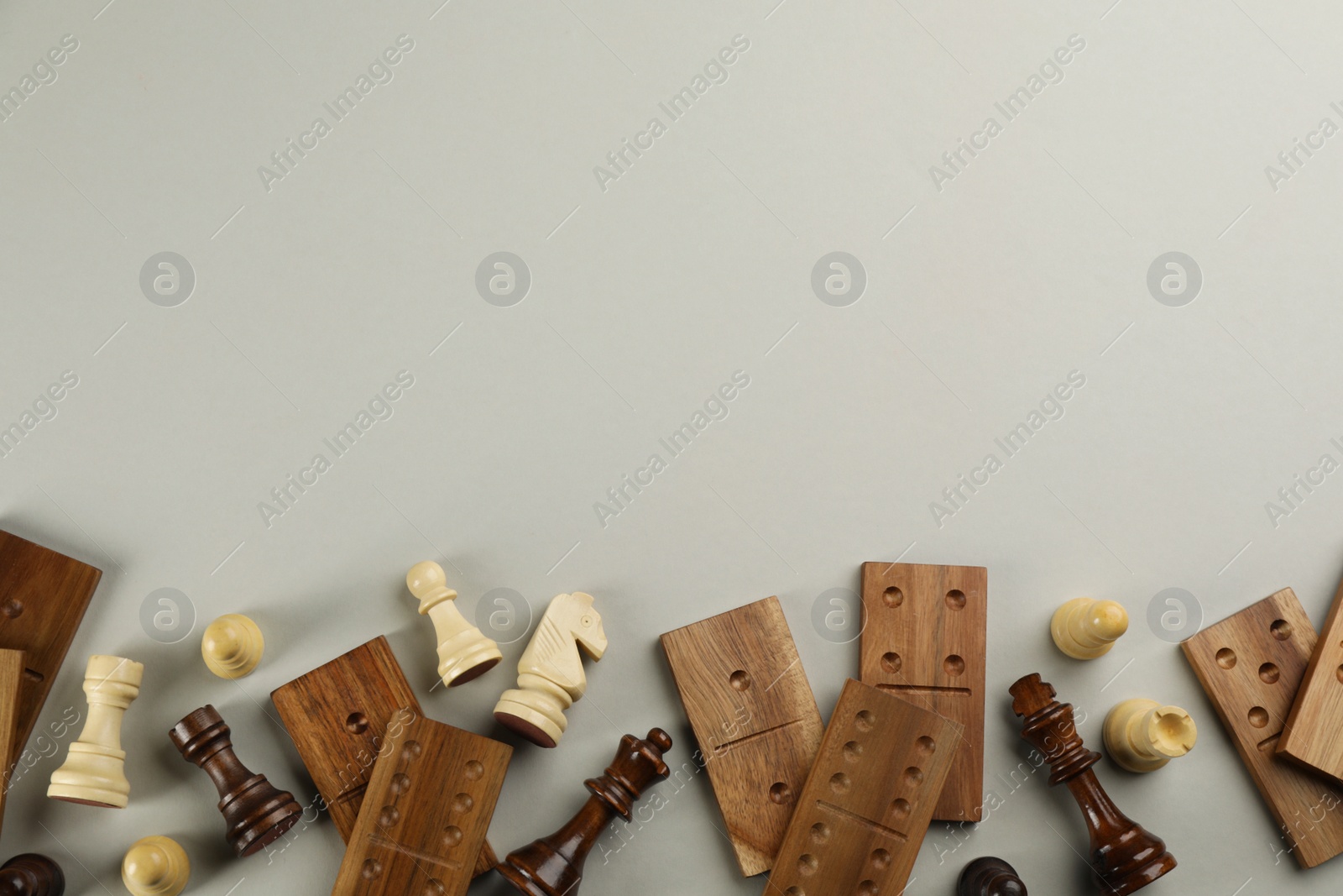 Photo of Chess pieces and domino tiles on grey background, flat lay with space for text. Board games components