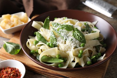 Delicious pasta with green peas, fresh basil and cheese on wooden table, closeup