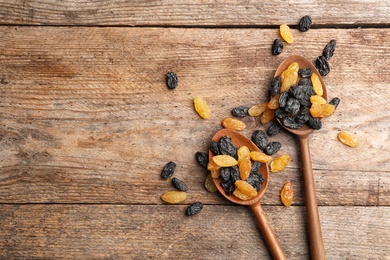 Photo of Spoons with raisins and space for text on wooden background, top view. Dried fruit as healthy snack