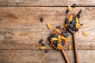 Spoons with raisins and space for text on wooden background, top view. Dried fruit as healthy snack