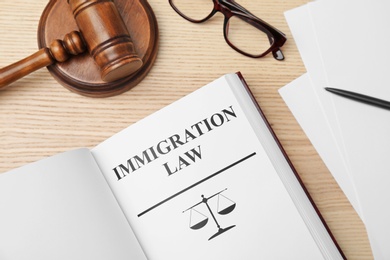 Photo of Book with words IMMIGRATION LAW, gavel and glasses on wooden background, top view