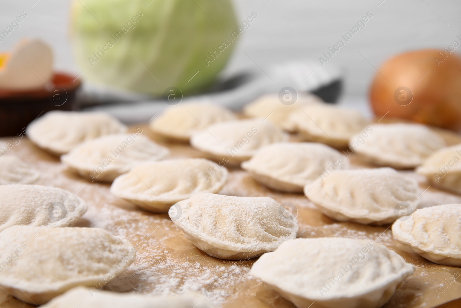 Photo of Raw dumplings (varenyky) with tasty filling and flour on parchment paper, closeup view