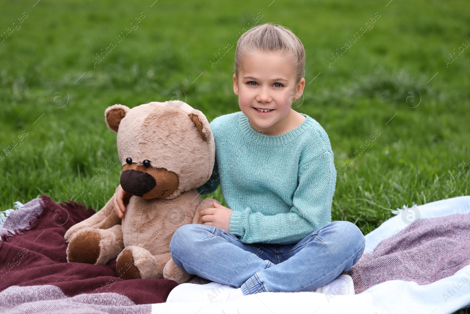 Photo of Little girl with teddy bear on plaid outdoors