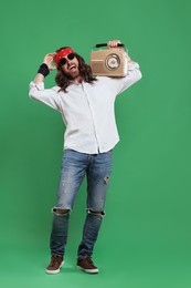 Stylish hippie man in sunglasses with retro radio receiver on green background
