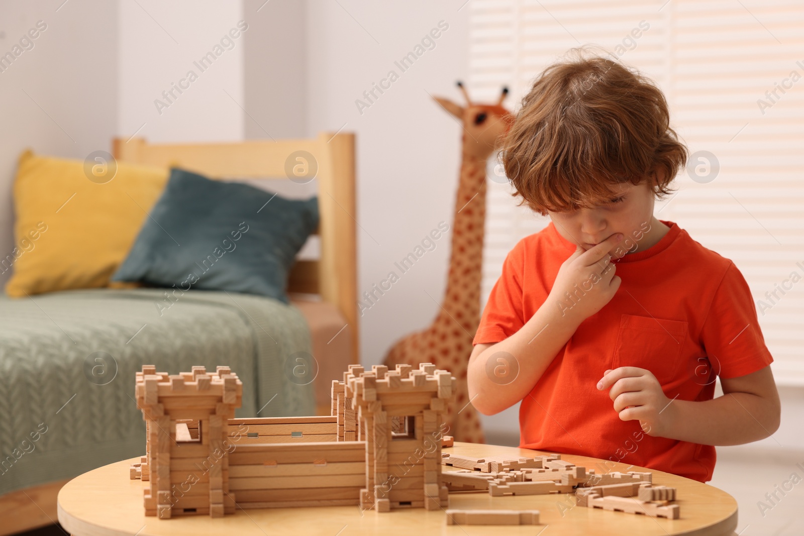 Photo of Little boy playing with wooden construction set at table in room. Child's toy