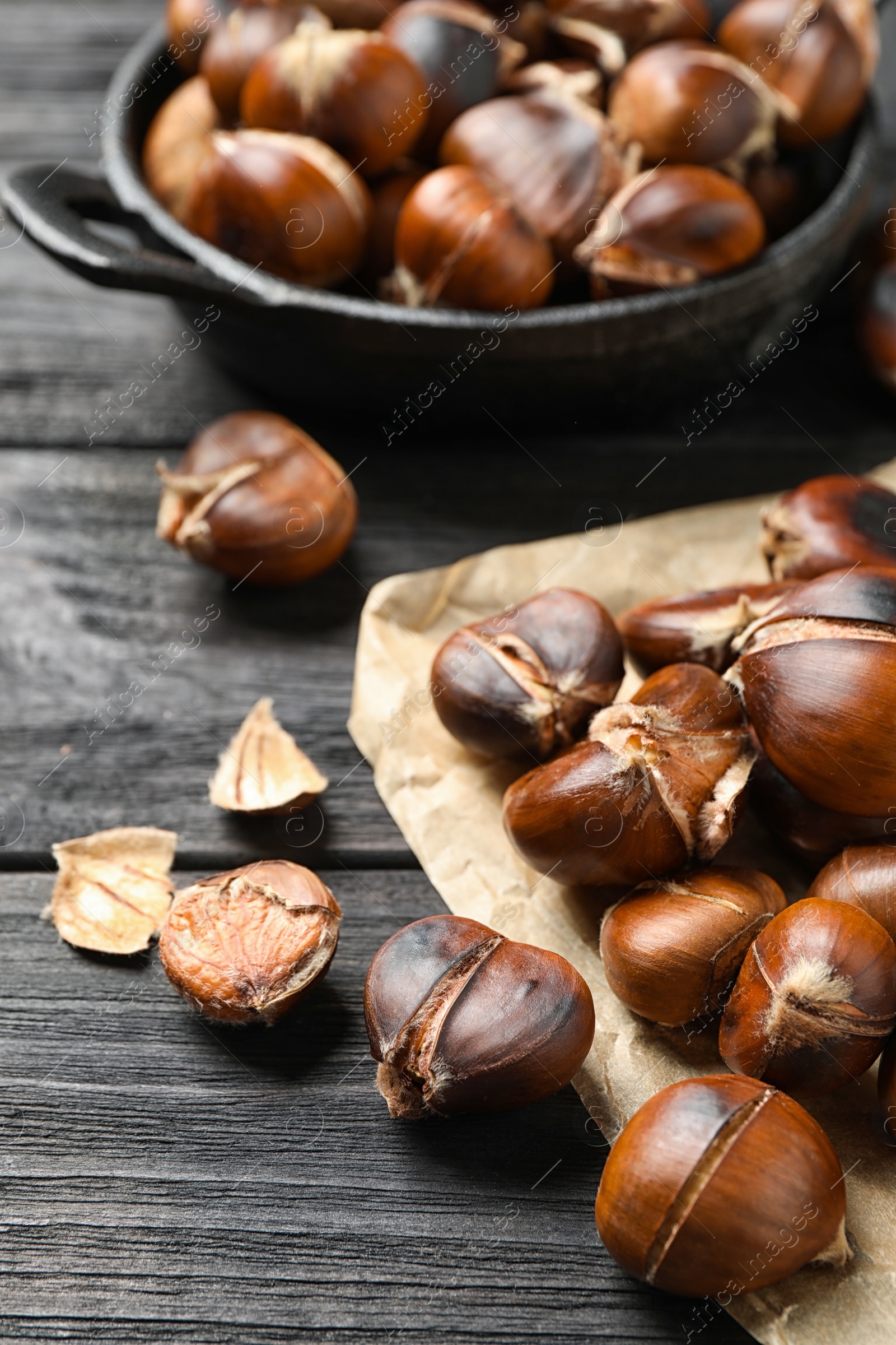 Photo of Tasty roasted edible chestnuts on black wooden table, closeup