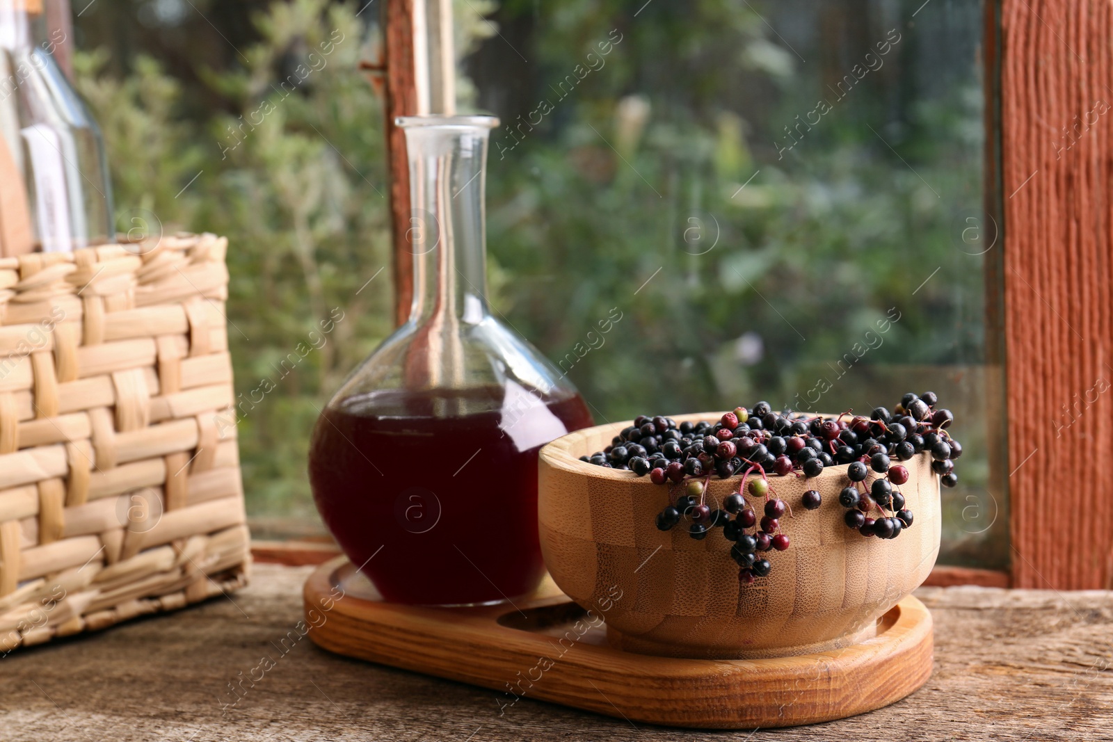 Photo of Elderberry wine and bowl with Sambucus berries on wooden table near window