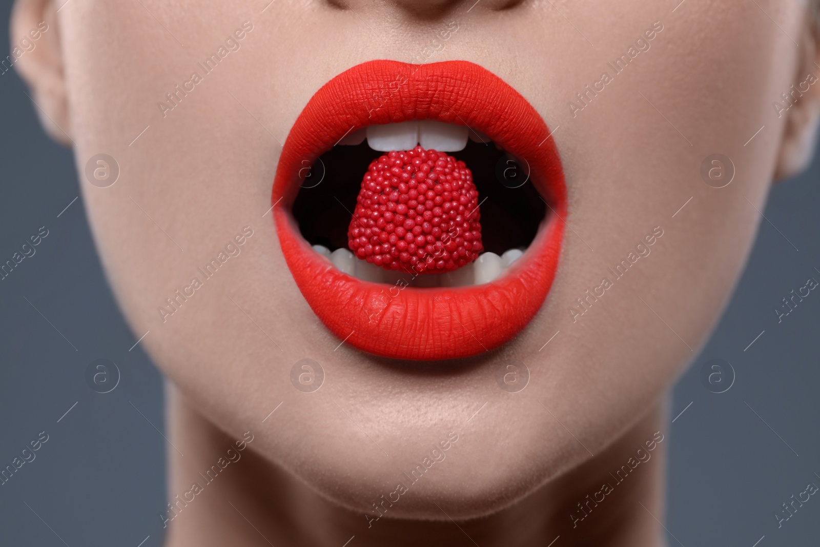 Photo of Young woman with beautiful red lips makeup eating candy on grey background, closeup