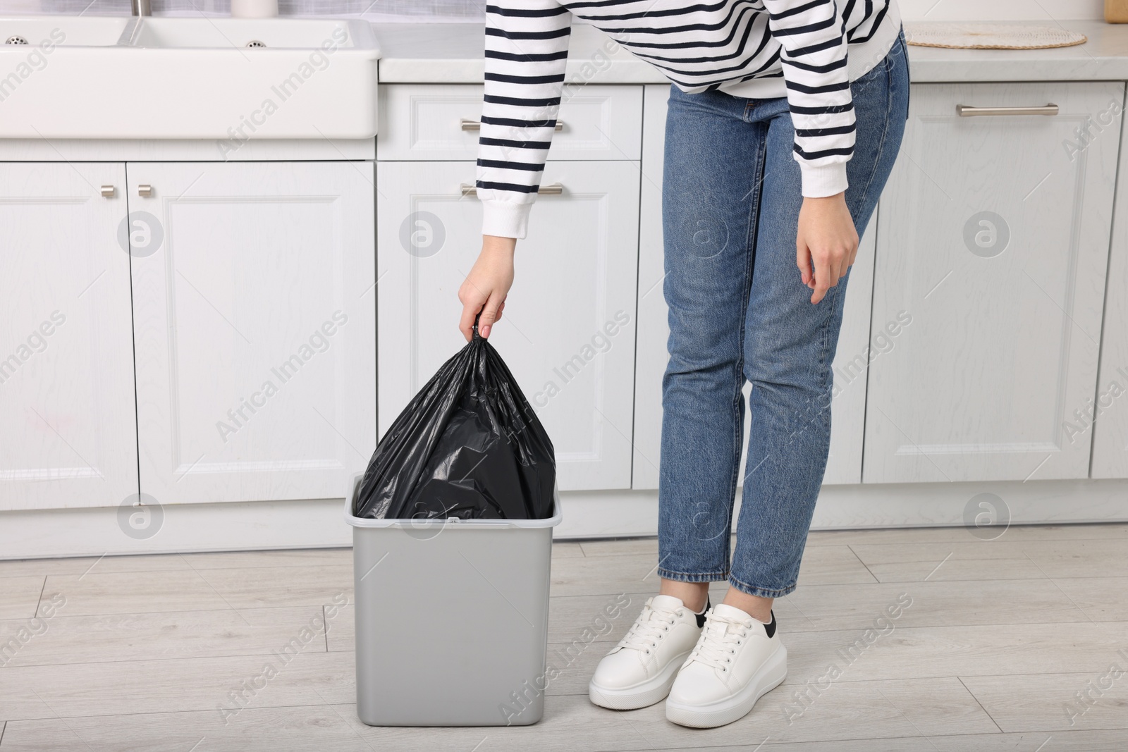 Photo of Woman taking garbage bag out of trash bin in kitchen, closeup