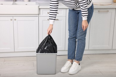 Photo of Woman taking garbage bag out of trash bin in kitchen, closeup