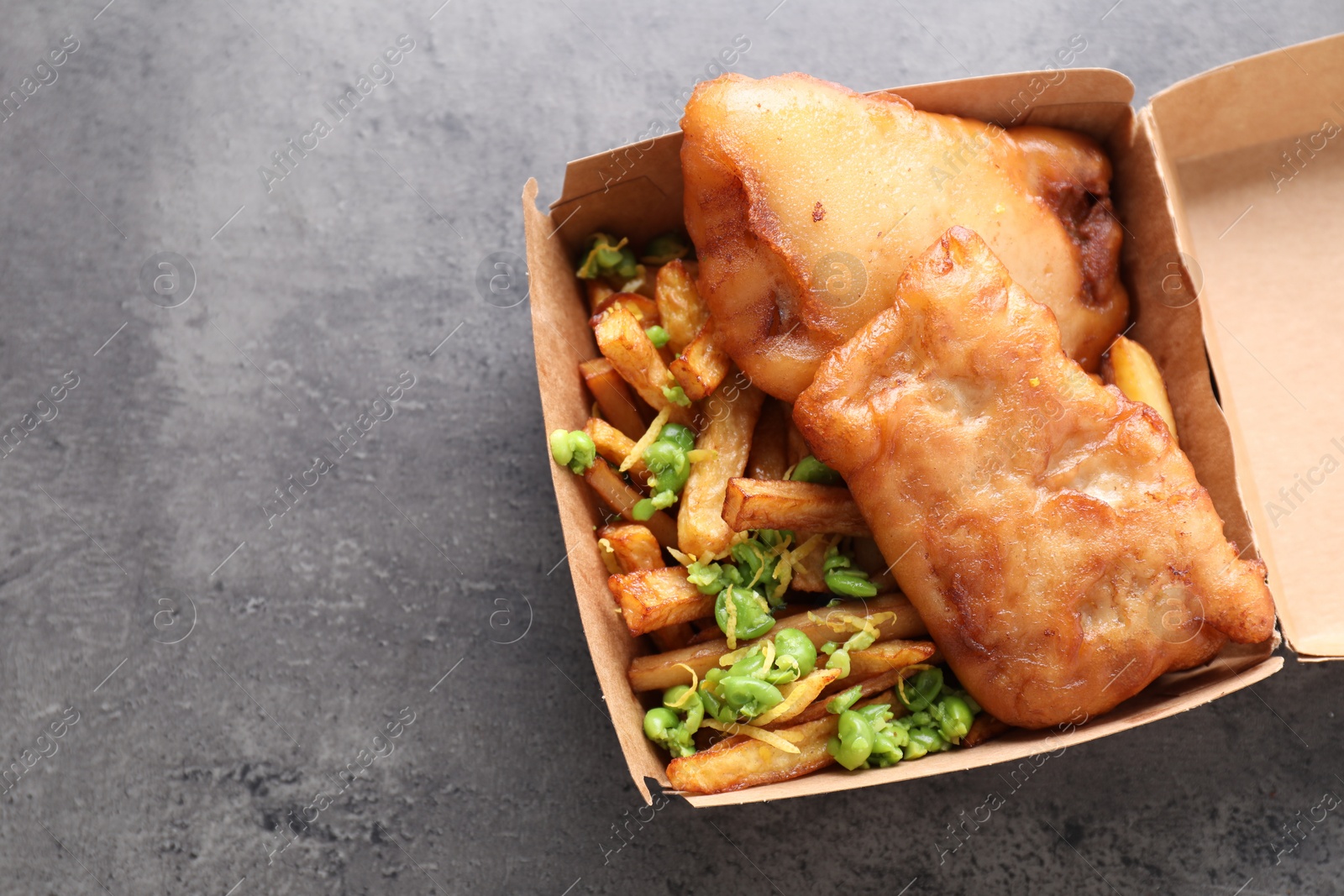 Photo of Tasty fish, chips and peas in paper box on grey table, top view. Space for text