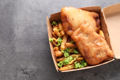 Photo of Tasty fish, chips and peas in paper box on grey table, top view. Space for text