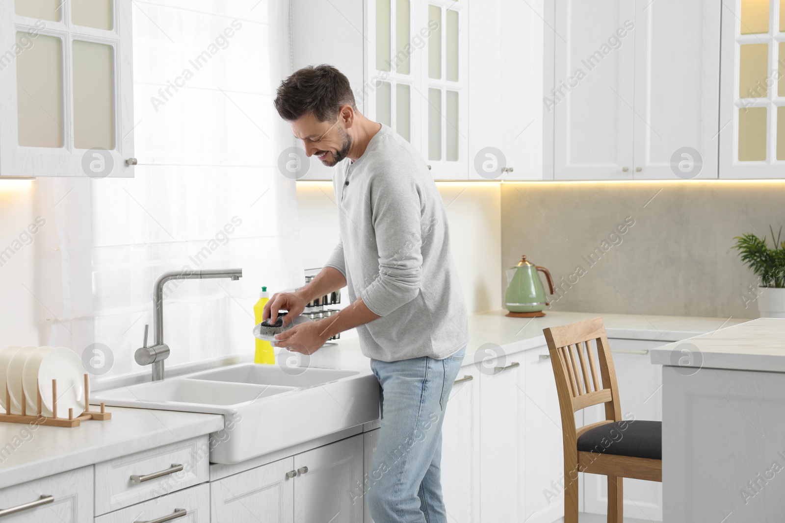 Photo of Man washing plate above sink in kitchen