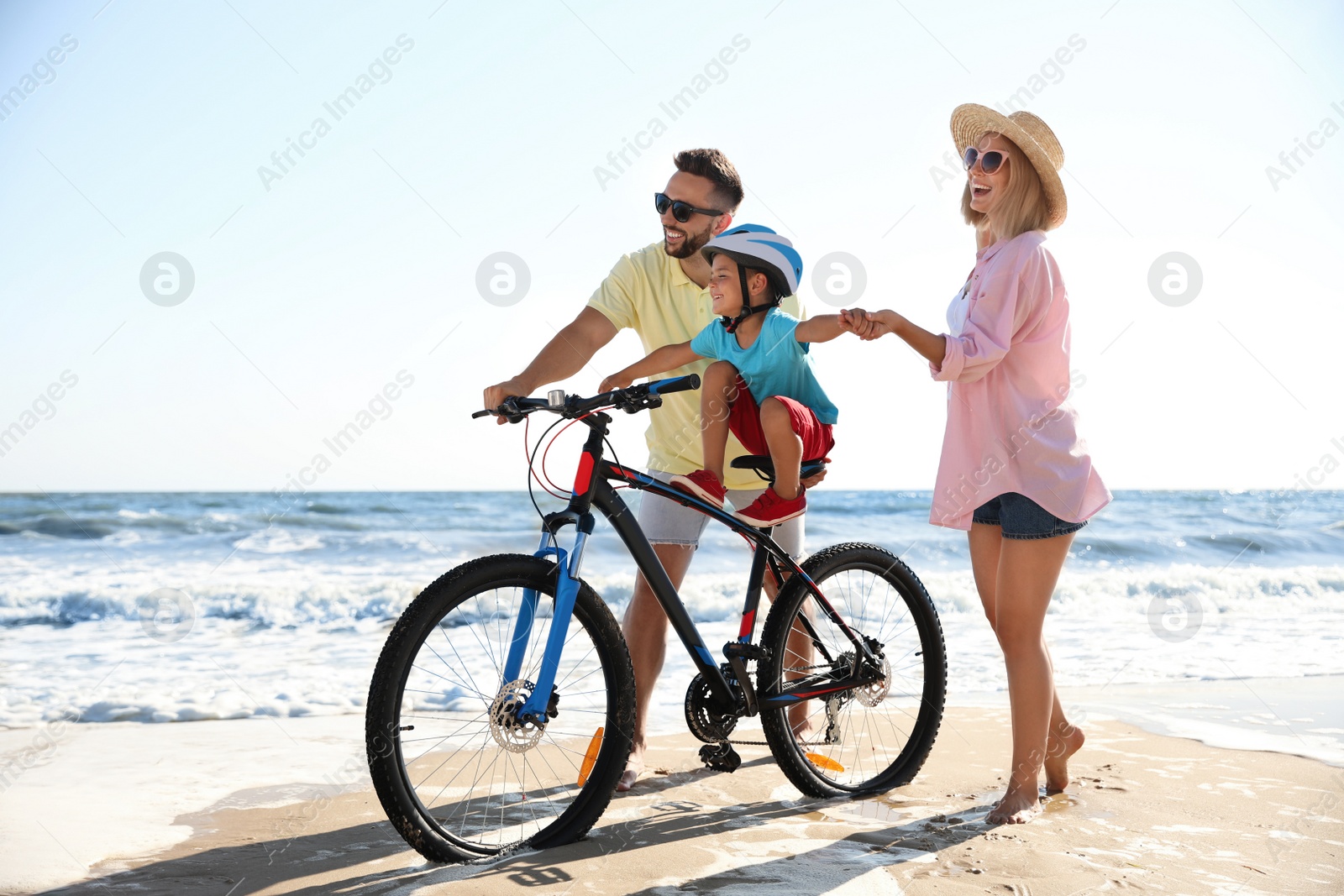 Photo of Happy parents teaching son to ride bicycle on sandy beach near sea