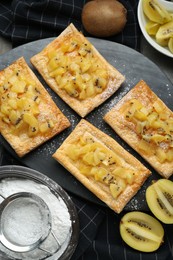 Fresh tasty puff pastry with sugar powder and kiwi served on grey table, flat lay