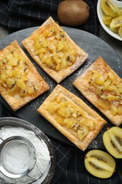 Photo of Fresh tasty puff pastry with sugar powder and kiwi served on grey table, flat lay