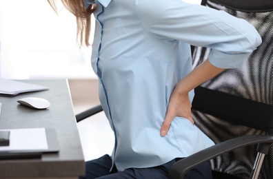 Photo of Young woman suffering from back pain in office, closeup