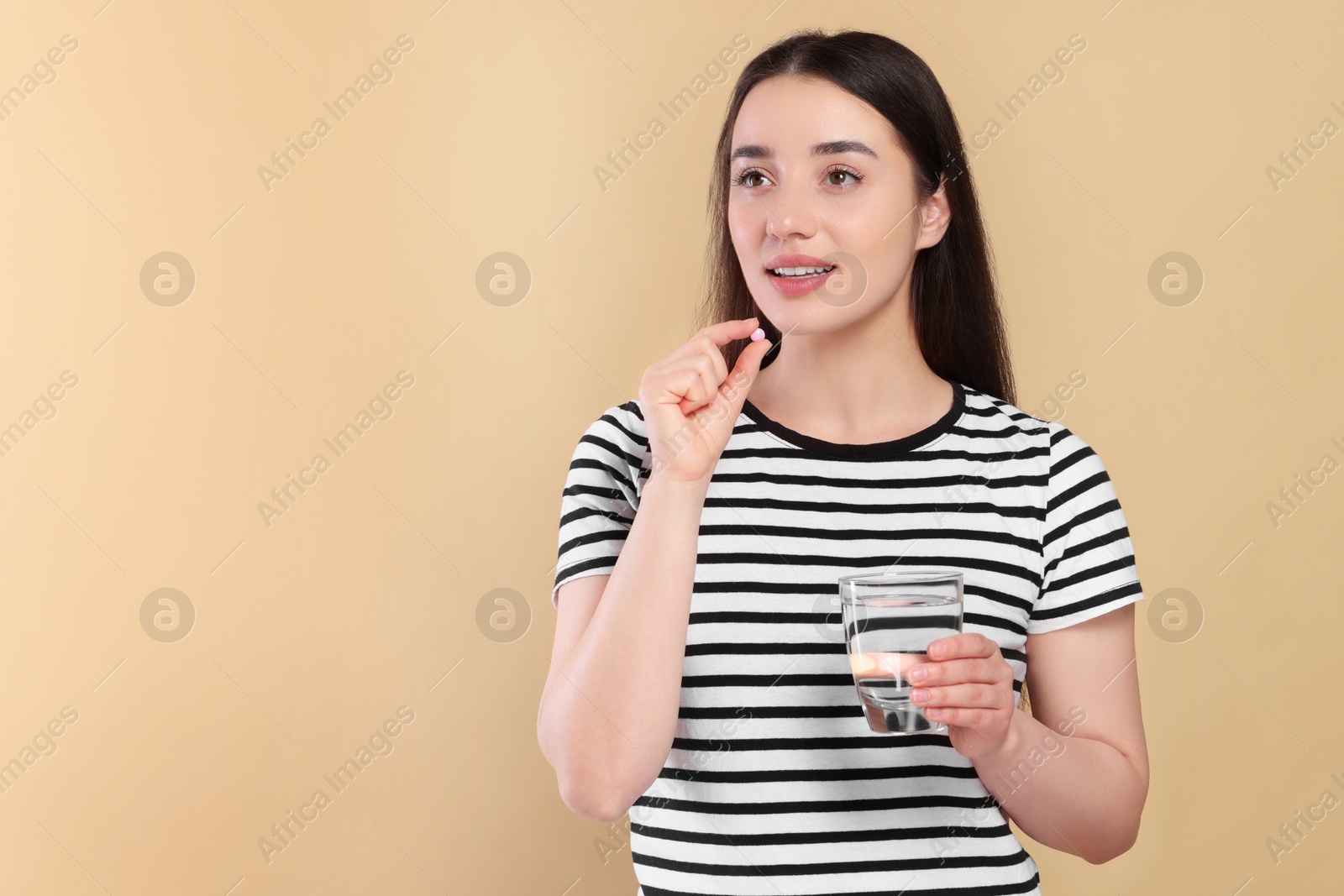 Photo of Happy woman with glass of water taking pill on beige background, space for text