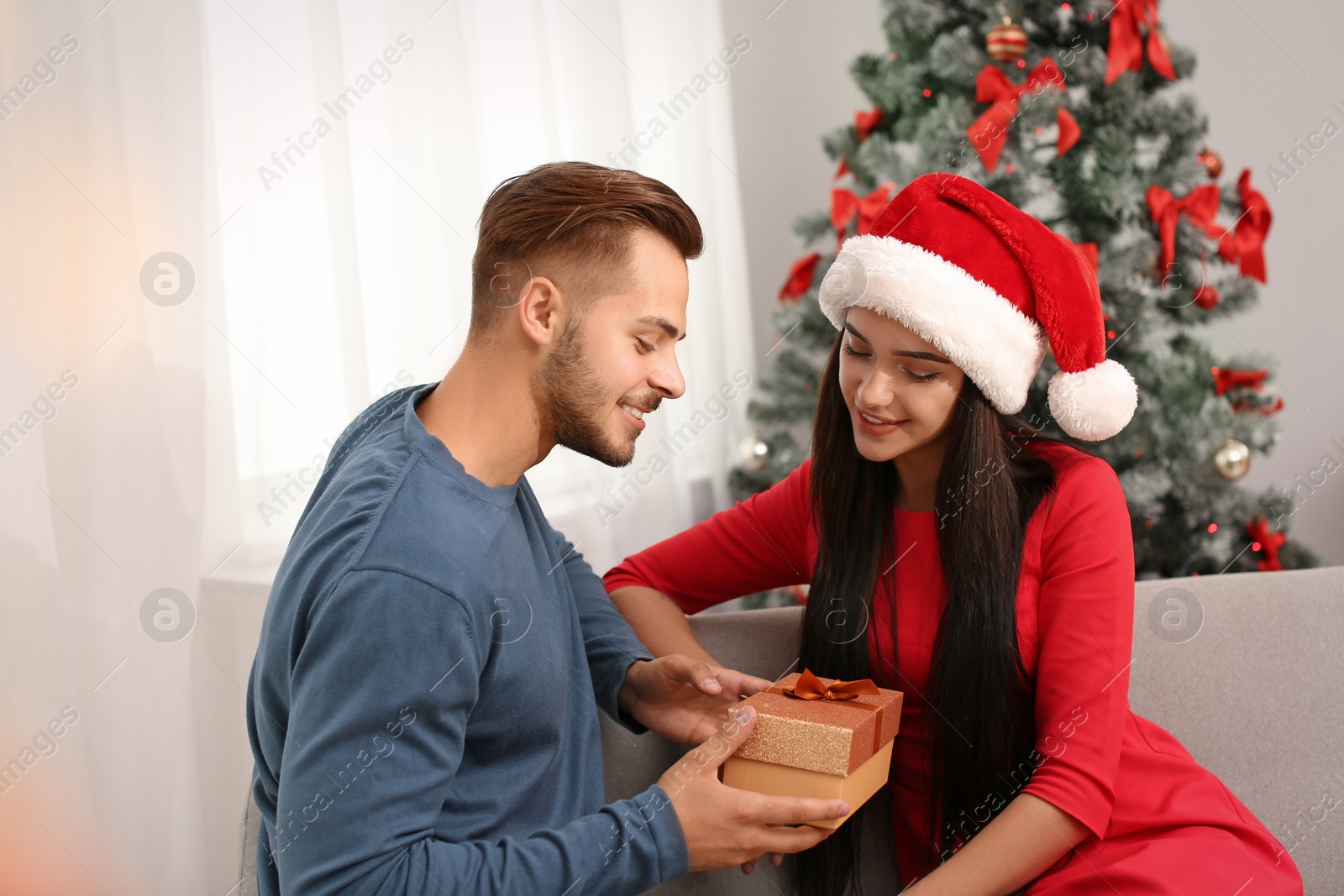 Photo of Young man giving gift box to woman at home. Happy couple celebrating Christmas