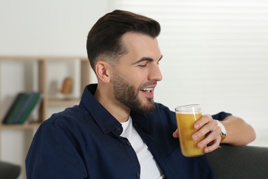 Photo of Handsome man with delicious smoothie on sofa at home