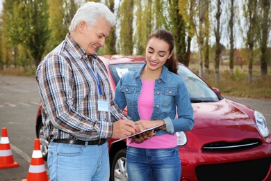 Senior instructor with clipboard and woman outdoors. Get driving license