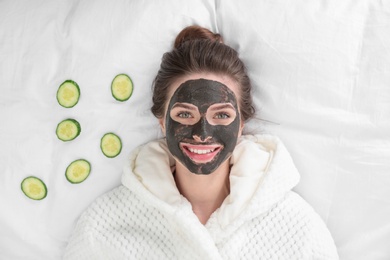 Photo of Young woman with facial mask lying and cucumber slices on bed, top view