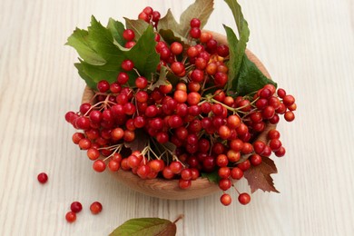 Photo of Bowl with tasty viburnum berries on white wooden table