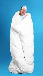 Photo of Man wrapped in blanket yawning on blue background