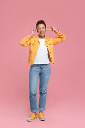 Photo of Happy young woman in headphones dancing on pink background