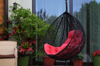 Photo of Comfortable swing chair with pink pillow near house. Garden furniture